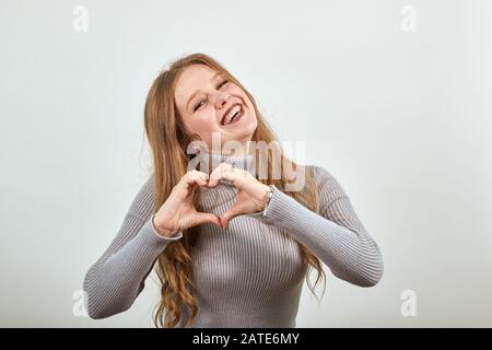 belle femme aux cheveux rouges dans un pull gris incline la tête et sourit avec bonheur Banque D'Images