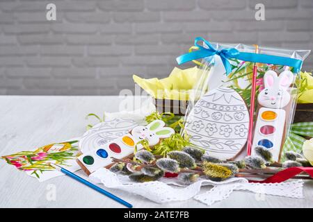 Vue de face de la peinture de cadeaux pour colorer les cocamies de pâques en forme d'oeufs, isolée sur table en bois. Peintures aquarelles près de la serviette, boîte avec fleurs, branche de saule, brosse. Concept de vacances de Pâques. Banque D'Images