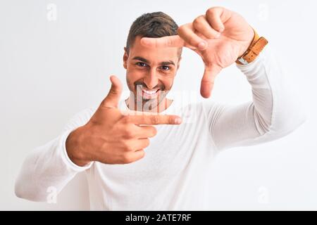Jeune homme portant une chemise blanche sur un arrière-plan isolé souriant faire le cadre avec les mains et les doigts avec le visage heureux. Créativité et photographie Banque D'Images