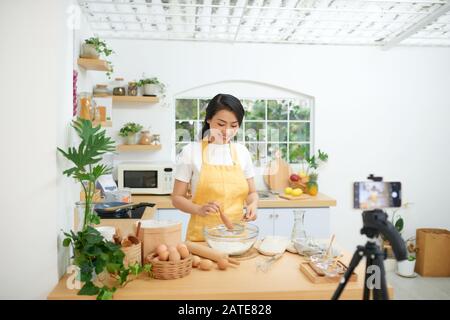 Jolie jeune femme d'origine asiatique food blogger travaille sur une nouvelle vidéo et d'expliquer comment cuisiner un plat Banque D'Images