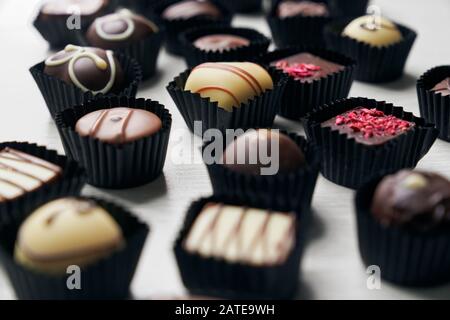 Foyer sélectif de bonbons au chocolat assortis dans des livres noirs isolés sur une table en bois blanc. Gros plan de délicieuses friandises colorées au goût différent. Concept de nourriture, bonbons. Banque D'Images