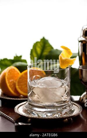 Un verre de whisky en cristal avec un grand morceau de glace sphérique et une garniture d'agrumes. Banque D'Images