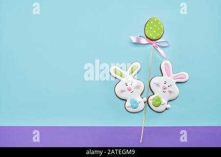 De la vue ci-dessus des cookies colorés au gingembre glacés isolés sur fond bleu et violet. Délicieuse pâtisserie maison en forme de lapins de pâques tenant des œufs. Concept de vacances, boulangerie. Banque D'Images