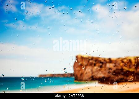 Une plage dorée et des falaises vues à travers une fenêtre couverte de raindrop. Banque D'Images