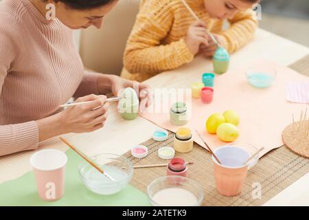 Portrait à grand angle de la mère et de la fille peindre des oeufs de Pâques couleurs pastel assis à la table dans une cuisine intérieure confortable, espace de copie Banque D'Images