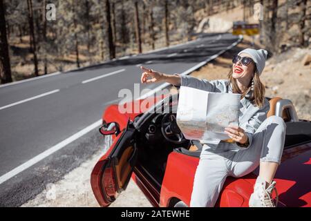 Femme en voyage sur route, assise avec carte sur la voiture convertible sur le bord de la route dans la forêt volcanique de montagne sur l'île de Tenerife, Espagne Banque D'Images