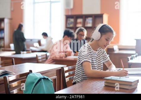 Étudiant d'université contemporain avec écouteurs écrivant le plan de séminaire Banque D'Images