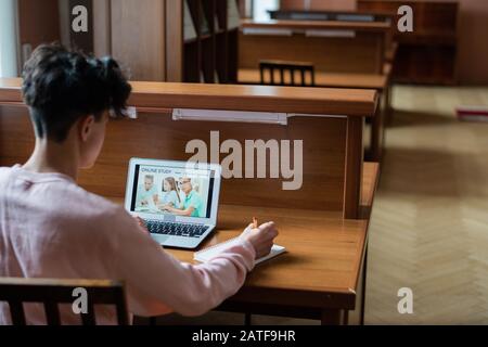 Vue arrière de l'étudiant contemporain assis à la réception devant un ordinateur portable Banque D'Images