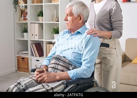 Homme handicapé âgé avec un verre d'eau assis sur le fauteuil roulant Banque D'Images