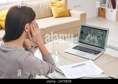 Jeune femme malade avec ses mains sur les temples ayant une consultation médicale en ligne Banque D'Images