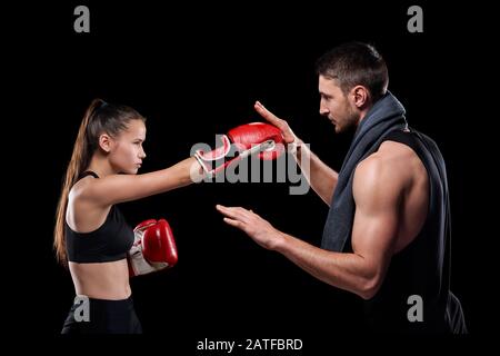 Jeune sportif dans l'activewear et gants de boxe exerçant avec l'entraîneur Banque D'Images