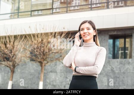 jeune femme d'affaires attrayante et confiante parlant au téléphone en face du centre d'affaires Banque D'Images