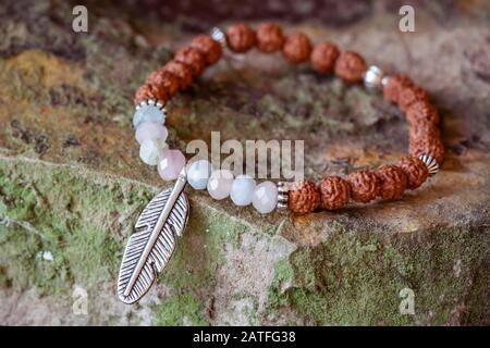 Bracelet en perles de graines de rudraksha en pierre minérale avec pendentif en plumes de métal sur fond rocheux Banque D'Images