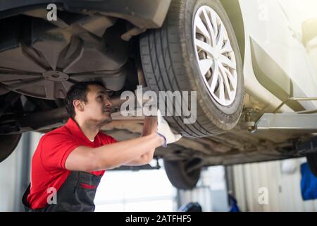 Un mécanicien de voiture professionnel travaillant sous une voiture levée lors d'un entretien de réparation automatique. Banque D'Images