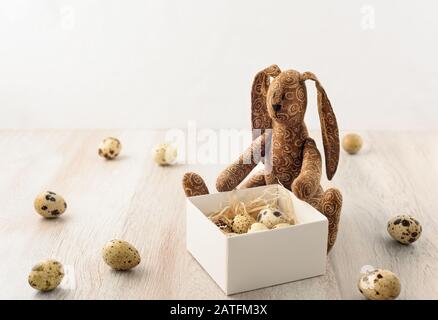 Le lapin de Pâques entouré d'œufs tient une boîte sur une surface en bois. Banque D'Images