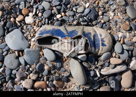 Une photo de la chaussure pour bébé abandonnée sur une plage rocheuse un après-midi ensoleillé. Banque D'Images