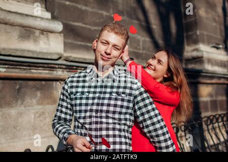 Accessoires de stand photo de la Saint Valentin. Femme cachant des accessoires en forme de coeur dans les cheveux de petit ami. Couple amoureux s'amuser Banque D'Images