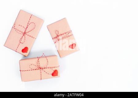 Boîtes cadeaux emballées dans du papier artisanal et décorées de ruban rouge et de coeurs en bois sur fond blanc. Saint Valentin, mariage ou autres décorations de vacances fond Banque D'Images