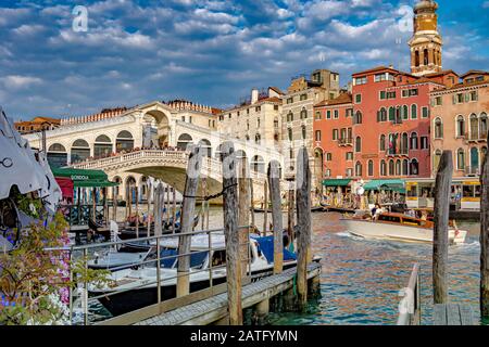 Un bateau-taxi sur le Grand Canal qui passe devant une jetée d'amarrage avec des bâtons d'amarrage en bois en direction du pont du Rialto, Venise, Italie Banque D'Images