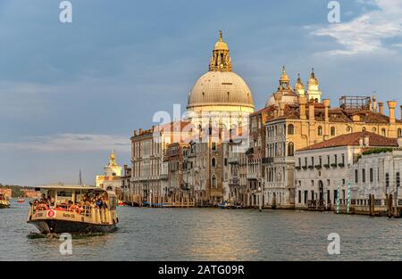 Un vaporetto ou un bateau-bus le font le long Du Grand Canal de Venise avec le dôme de la basilique Santa Maria della Salute en arrière-plan Banque D'Images