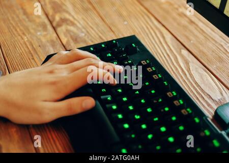 Jeu d'ordinateurs. Gros plan des mains mâles sur un clavier de jeu noir avec lumière néon sur une table en bois. Banque D'Images