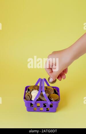 Main tenant une pièce de monnaie avec pile de pièce dans le panier d'achat sur fond jaune Banque D'Images