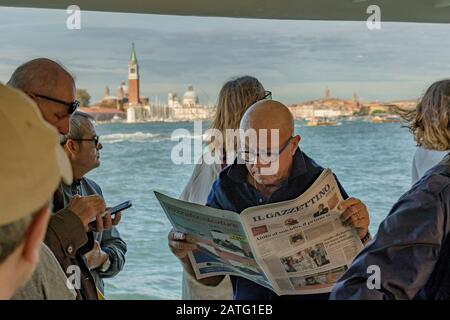 Un homme qui lit un journal à côté d'autres passagers sur un vaporetto ou un service de bateaux-bus sur La lagune de Venise, sur la route de Venise, Italie Banque D'Images