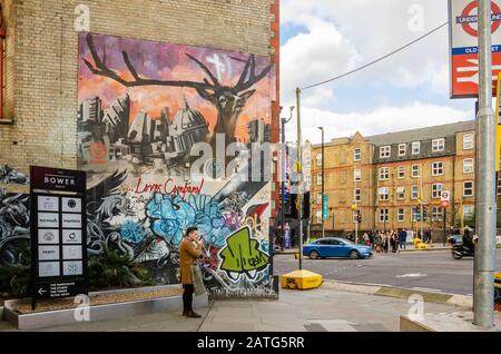 L'homme se tient debout et utilise son téléphone portable devant des œuvres d'art colorées sur un coin de City Road à Londres, à côté d'une entrée à la gare de Old Street Banque D'Images