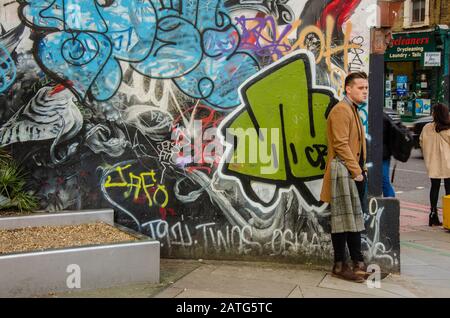 Un homme se tient sur un coin de rue devant des œuvres d'art colorées et des graffitis. Banque D'Images