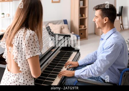 Femme enseignant au jeune homme en fauteuil roulant pour jouer au piano Banque D'Images