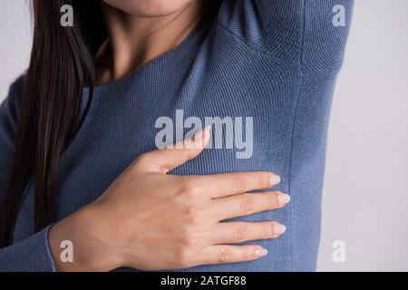 Gros plan femme asiatique avec l'hyperhidrose la transpiration. Jeune femme d'Asie de sueur tache sur ses vêtements contre un arrière-plan gris. Concept de soins de santé. Banque D'Images