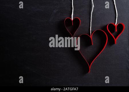 Coeurs en papier rouge accrochés sur des cordes sur fond noir. L'amour et le concept de Saint Valentin. Banque D'Images