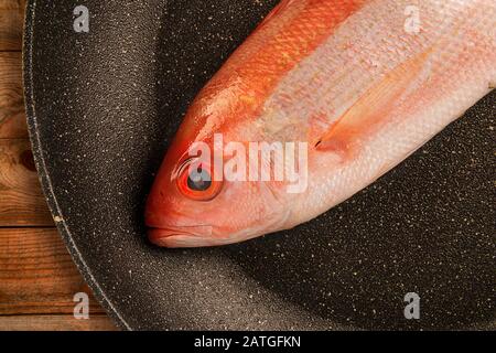 Poisson cru vivaneau rouge isolé éliminé dans une poêle à frire. Table en bois en arrière-plan. Banque D'Images