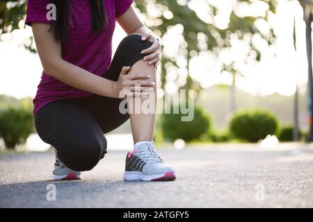 Jeune femme fitness runner ressentir la douleur sur son genou dans le parc. Les activités de l'exercice en plein air concept. Banque D'Images