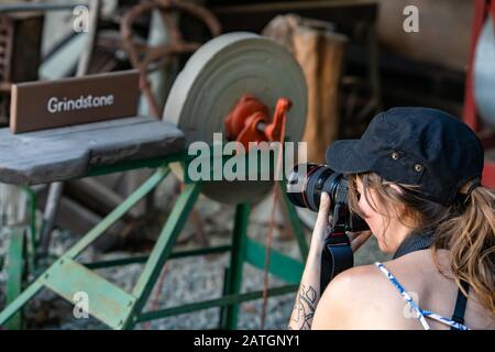 Visiteur prenant des photos de machinerie ancienne en pierre à affûter dans le musée, Kootenays, Colombie-Britannique, Canada. Un photographe prend des photos avec un appareil photo reflex numérique Banque D'Images