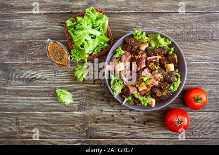 Salade chaude et saine de foie de poulet, de croutons de seigle, de bacon fumé, de salade verte et de sauce moutarde dans un bol sur fond de bois Banque D'Images
