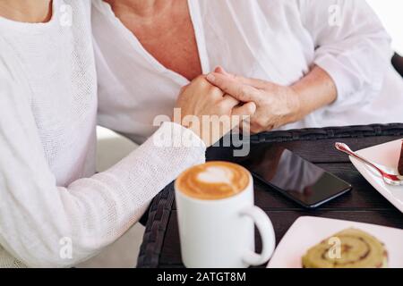 Image rapprochée de la fille rassurant sa mère et tenant sa main quand ils boivent du café ensemble Banque D'Images