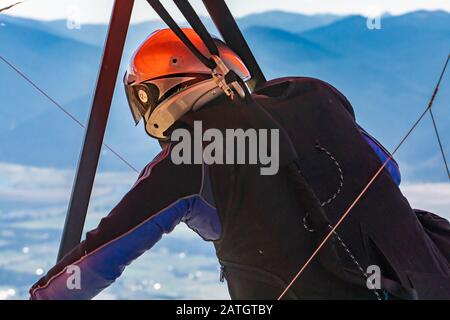 Vue rapprochée du pilote du planeur suspendu dans un équipement spécial et des vêtements prêts à voler. Montagnes de la vallée de Kootenay en arrière-plan Banque D'Images