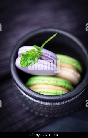 Macarons de lavande et de menthe française maison ou macarons dans une tasse noire sur fond sombre Banque D'Images