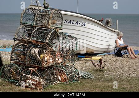 femme lisant à lee de bateau de pêche longishore sizewell suffolk angleterre Banque D'Images