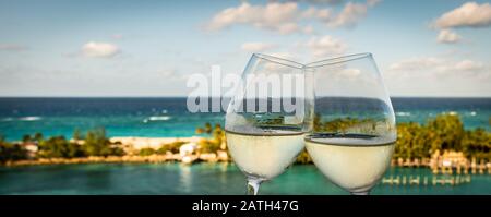Image large avec un gros plan de deux verres à clinking de vin blanc extérieur. Mer et fond d'île au port de Nassau aux Bahamas. Banque D'Images