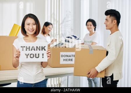 Jolie jeune femme vietnamienne travaillant comme bénévole au centre de donation et montrant carte de remerciement jeune Banque D'Images