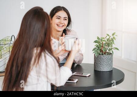 Jeune fille brunette insouciante amis dans une ambiance décontractée avec des tasses de thé dans un café lumineux ou une cuisine avec des plantes vertes sur la table Banque D'Images