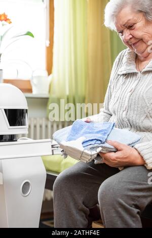 le robot autonome de soignant tient deux serviettes, les donnant à une femme adulte senior dans son salon, concept de vie assistée d'ambiance Banque D'Images