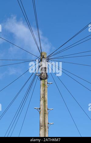 Fils téléphoniques rayonnant du poteau en bois dans la rue urbaine, avec fond bleu ciel Banque D'Images