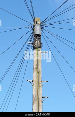 Fils téléphoniques rayonnant du poteau en bois dans la rue urbaine, avec fond bleu ciel Banque D'Images