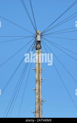 Fils téléphoniques rayonnant du poteau en bois dans la rue urbaine, avec fond bleu ciel Banque D'Images