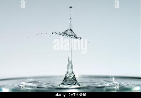 Les gouttes d'eau forment des sculptures transparentes fascinantes lorsqu'elles tombent dans de l'eau claire bleu clair, des gouttes et des éclaboussures se ferment. Banque D'Images