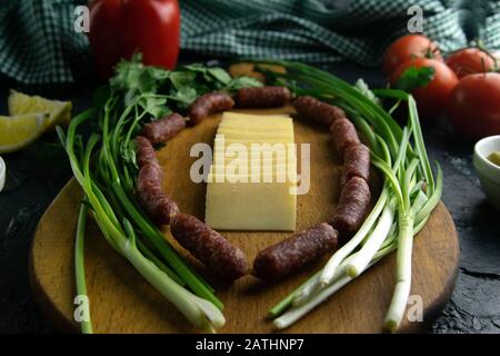 Tranches de fromage sur une planche en bois, autour du jambon, oignons verts, tomate, souce, olives, citron, épices, aneth. Banque D'Images