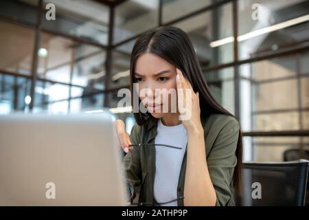 Brunette asiatique à poil long qui travaille au bureau et souffre d'un mal de tête Banque D'Images